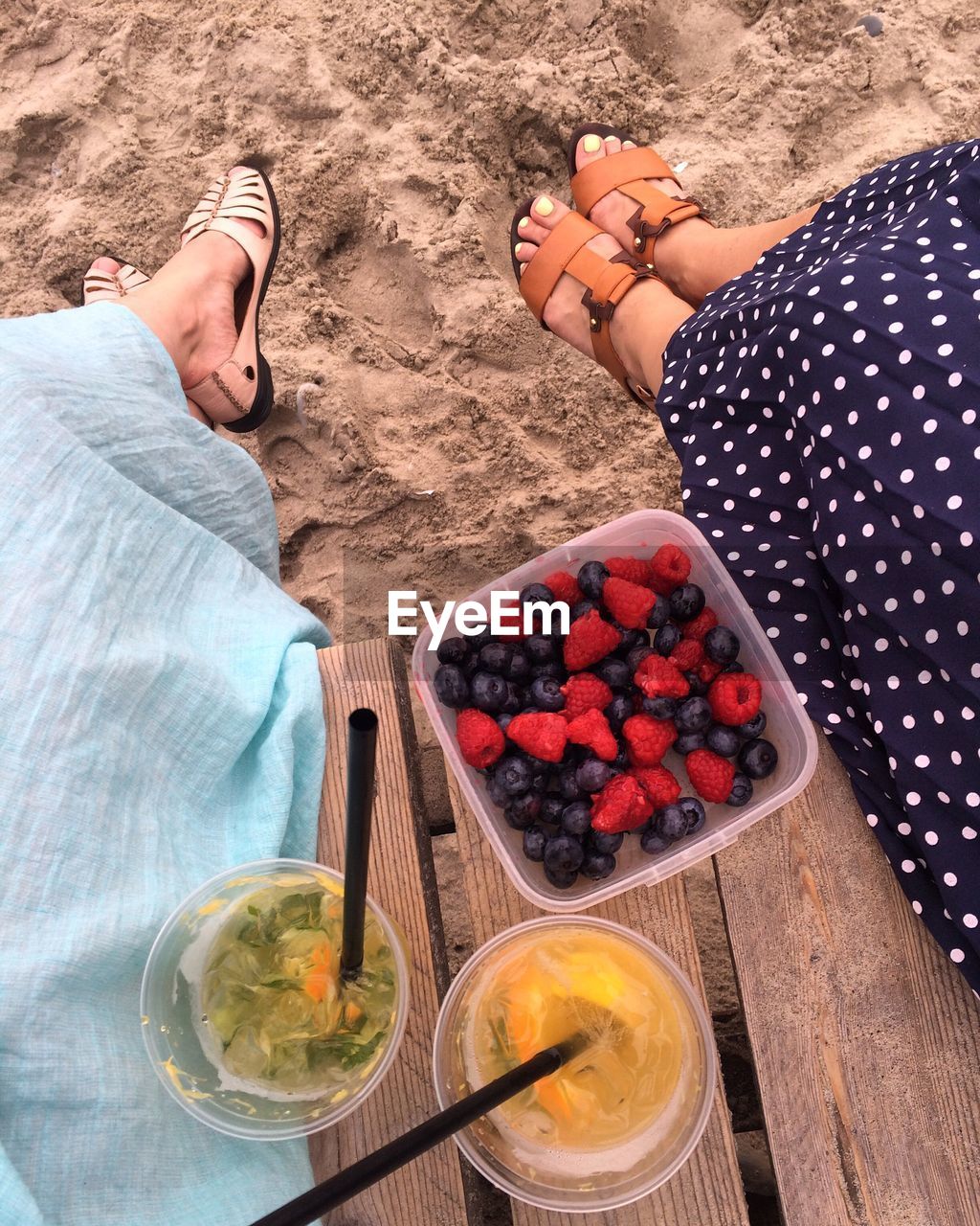 Low section of women sitting by fruits in container at beach