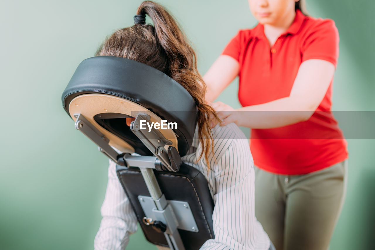 Female employee sitting on a portable massage chair in business office. therapist massaging 