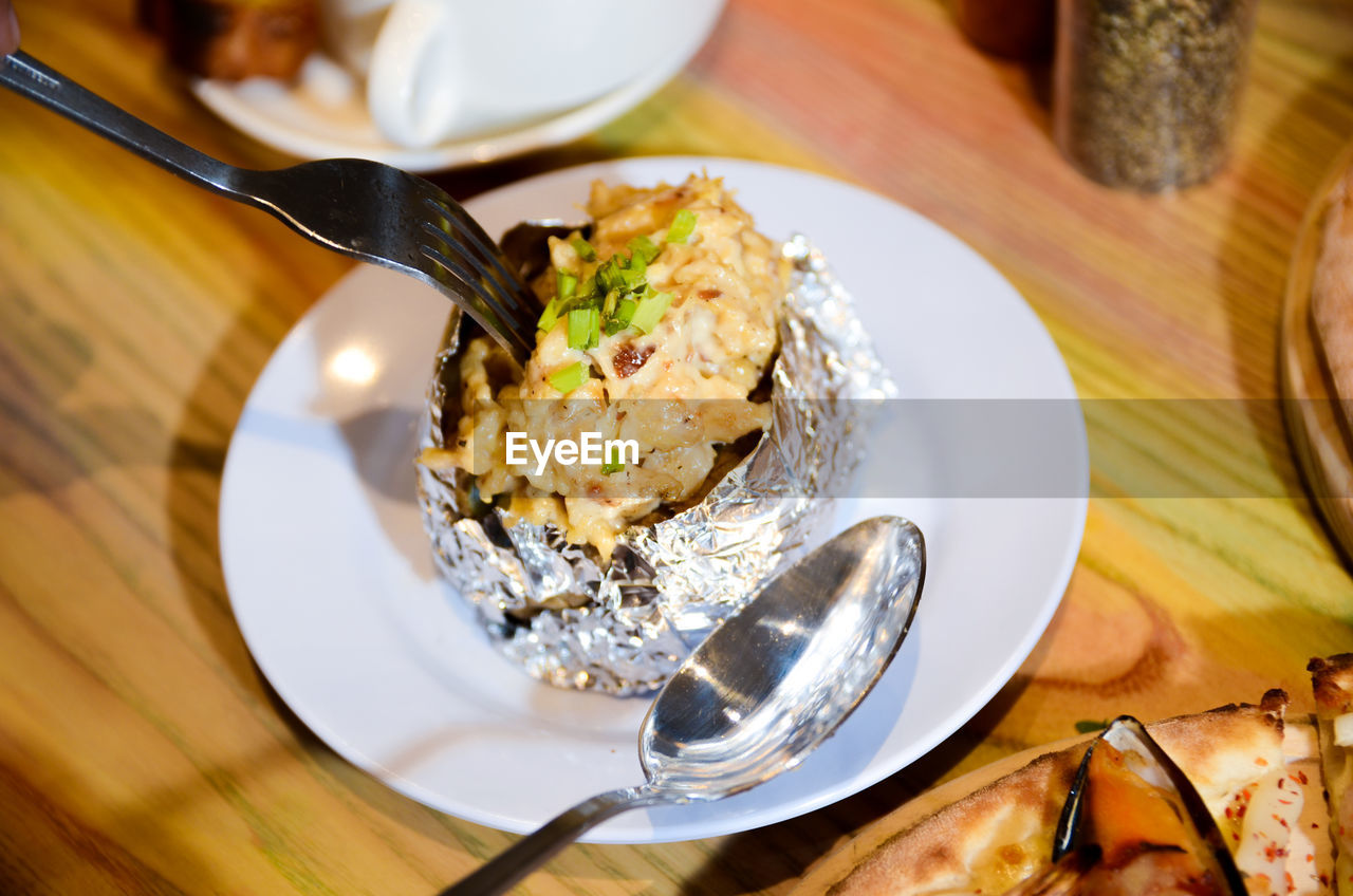 Woman eating baked mash potato wrap with aluminium foil. lunch, dinner at restaurant