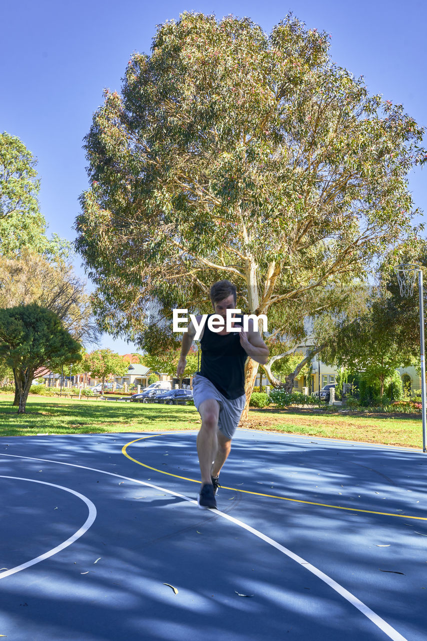 Full length of man running on court against tree