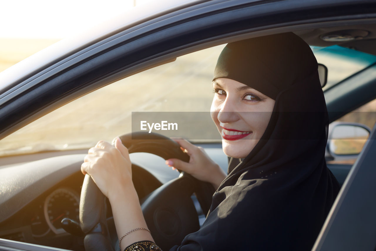 Portrait of woman wearing hijab driving in car seen through window
