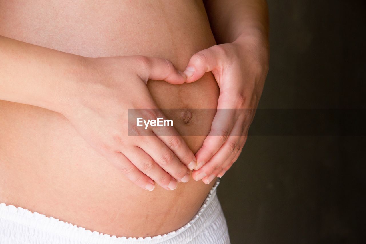 Midsection of pregnant woman making heart shape on belly