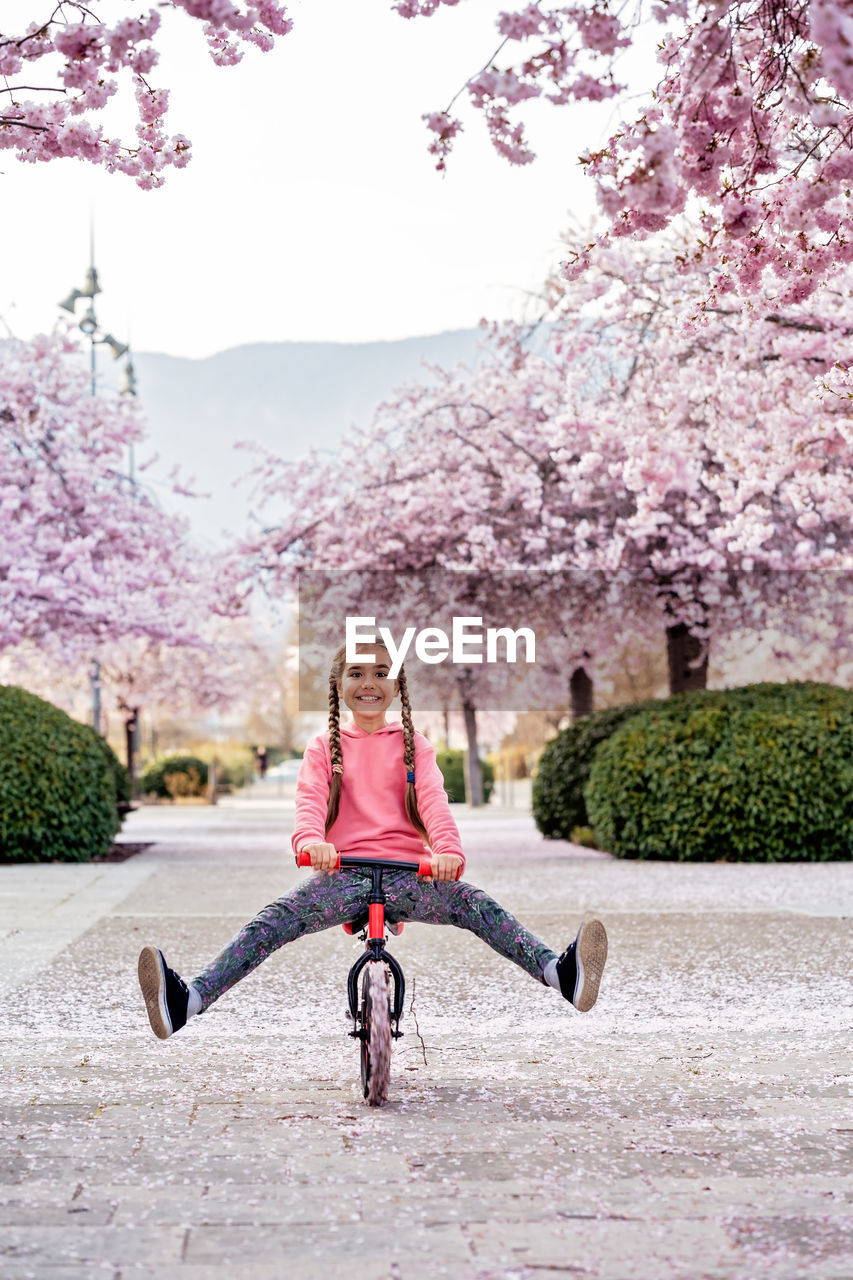 Happy smiling girl riding balance bike with her legs up on bloomimg spring sakura alley