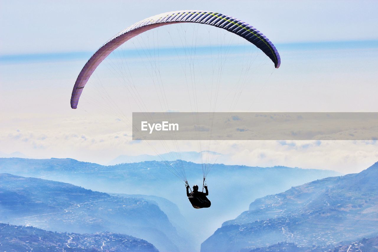 LOW ANGLE VIEW OF PERSON PARAGLIDING AGAINST MOUNTAIN