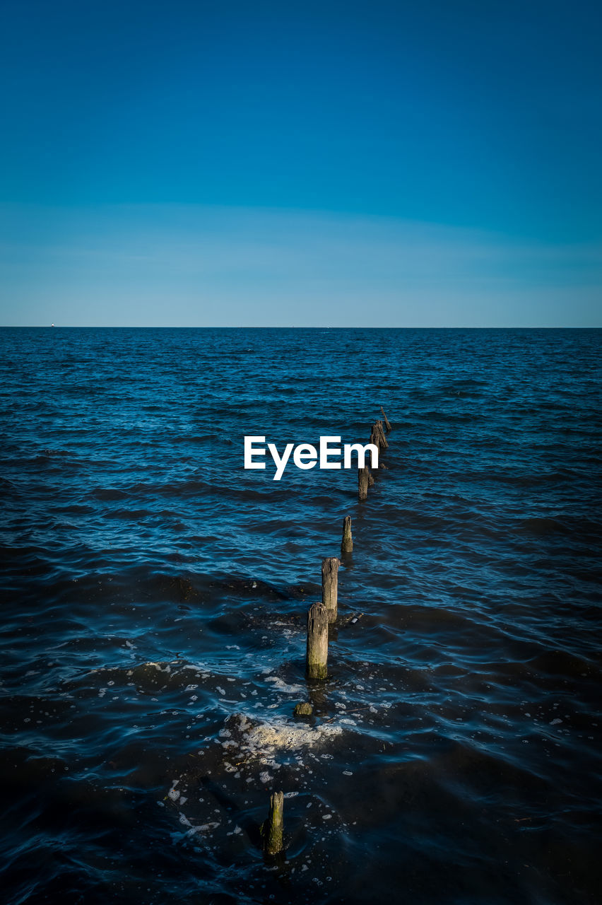 High angle view of wooden posts amidst sea against clear blue sky