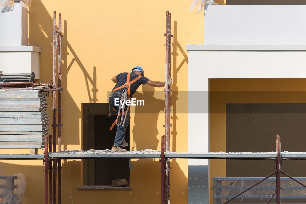 MAN WORKING AT CONSTRUCTION SITE AGAINST BUILDINGS