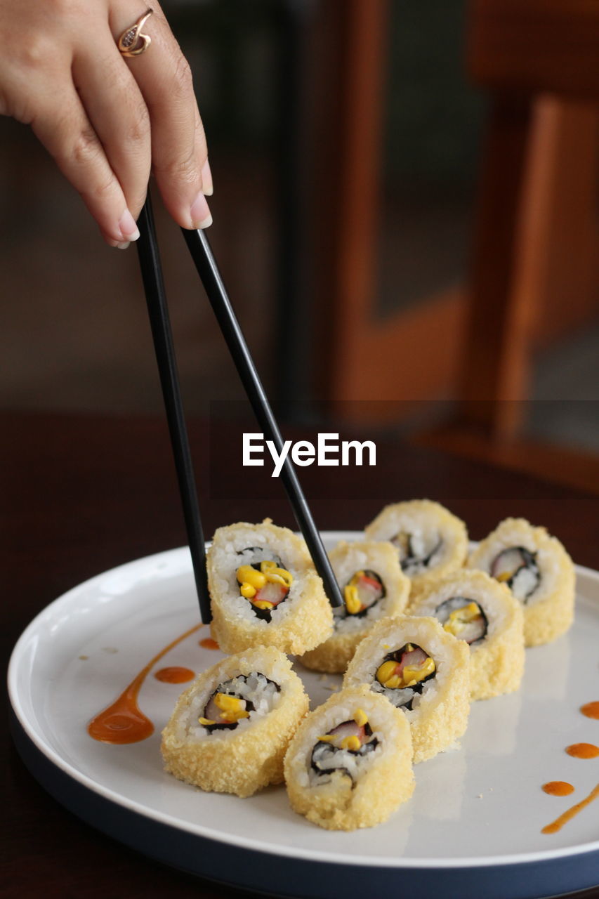 Close-up of woman hand holding sushi in plate on table