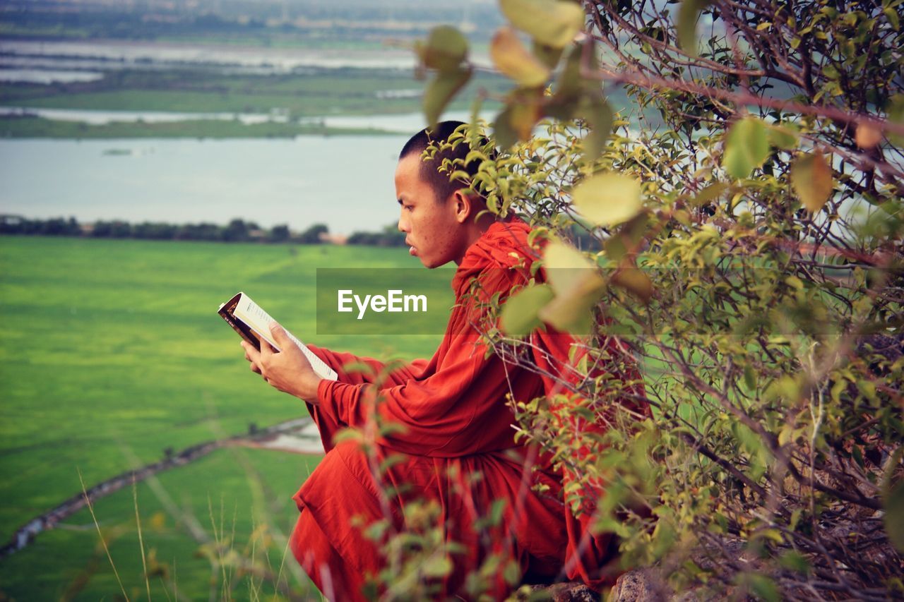 Side view of monk reading book on field