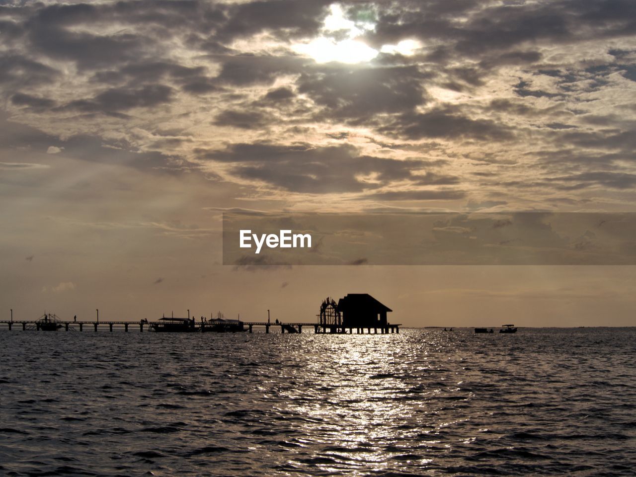 Silhouette hut in sea against sky during sunset