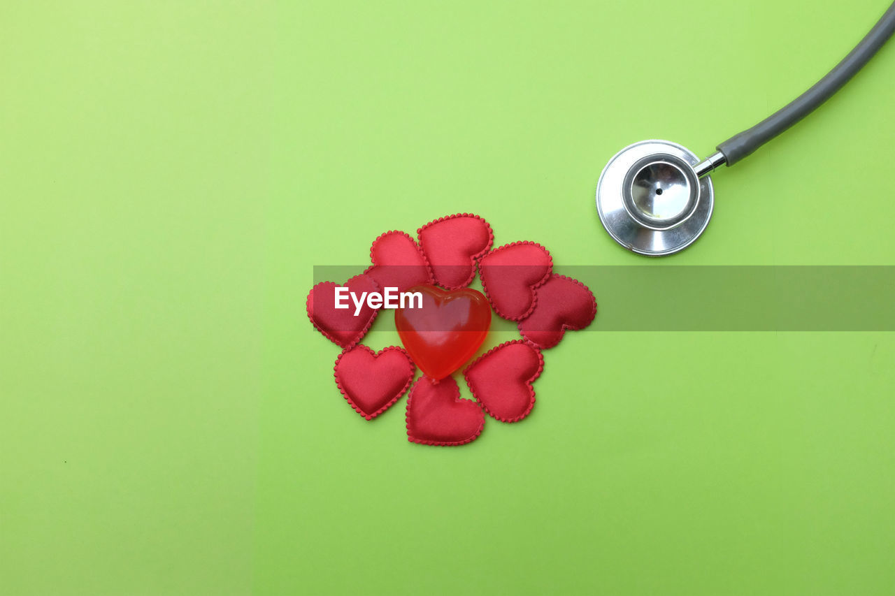 Close-up of red heart shapes by stethoscope against green background