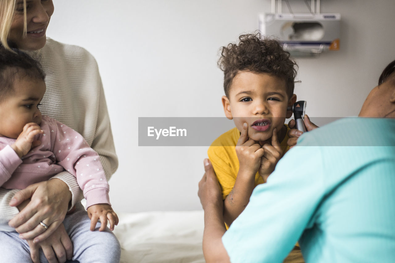 Portrait of boy making faces during ear examination by female doctor in clinic