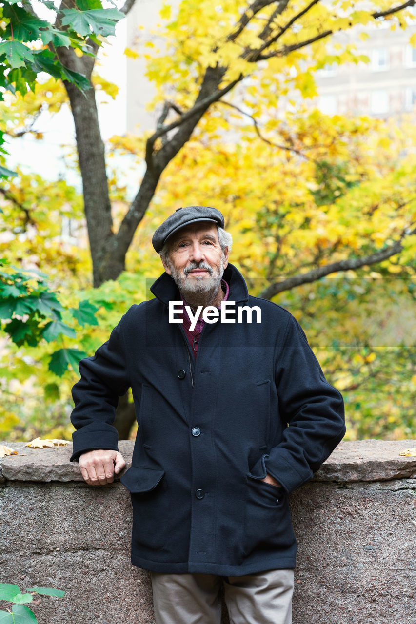 Portrait of confident senior man standing with hand in pocket in park during autumn