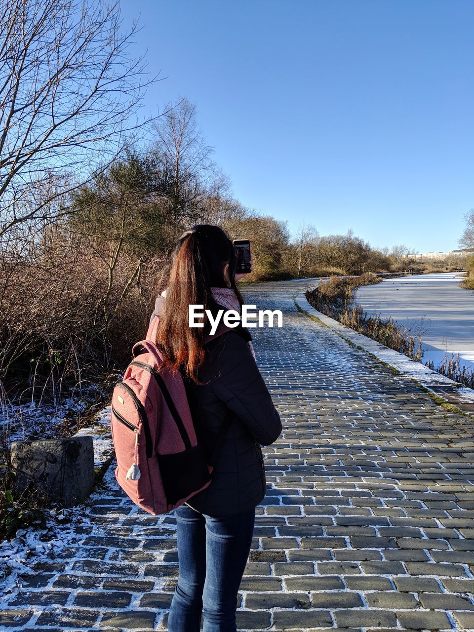 Rear view of woman standing on a riverside footpath against sky