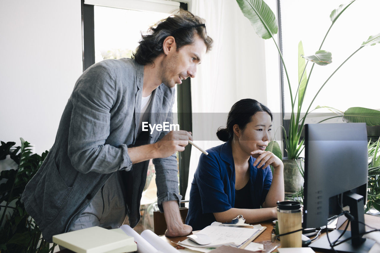 Male architect discussing with female colleague using computer at home office