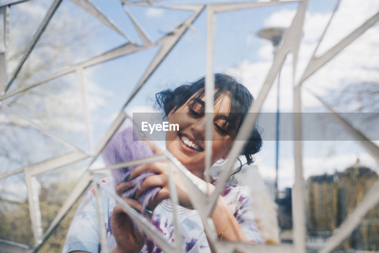 Reflection of young woman using mobile phone against glass mosaic wall