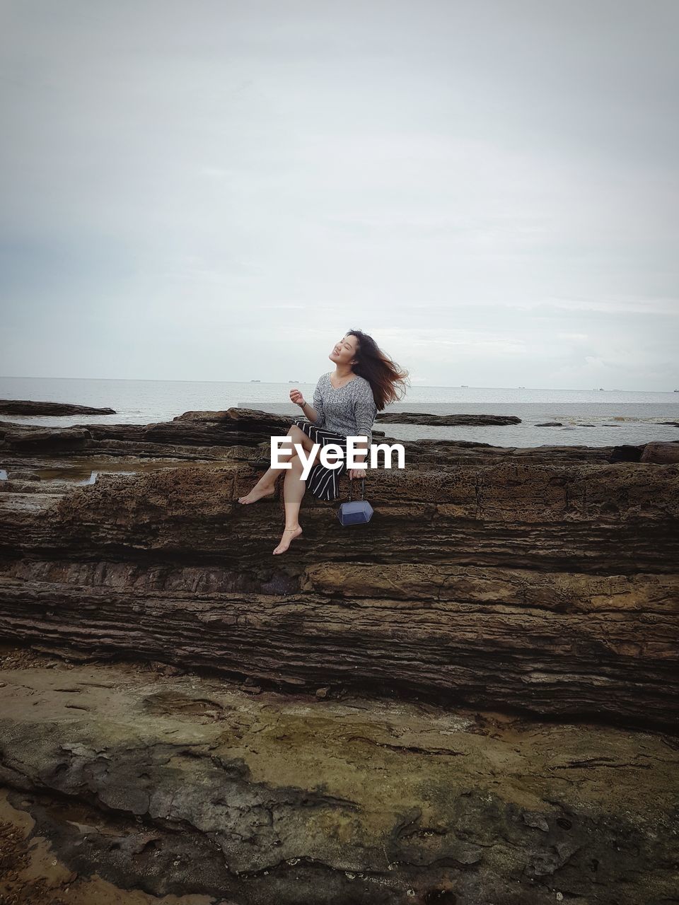 Smiling woman sitting on cliff against cloudy sky