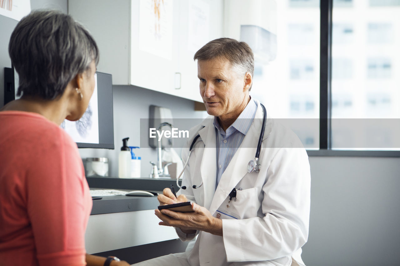 Male doctor writing in note pad while discussing with female patient in clinic