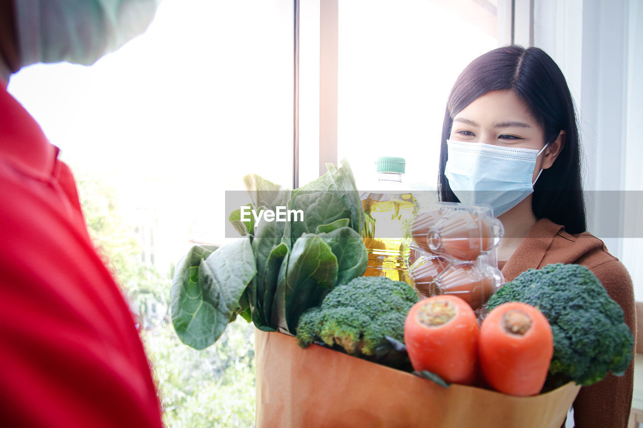 Smiling woman wearing mask taking delivery of vegetables at home