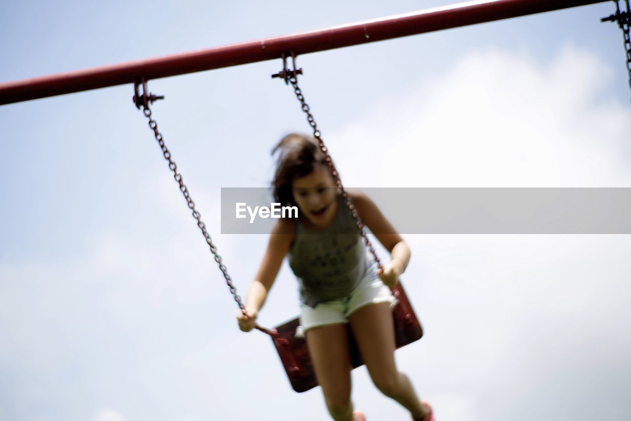 Low angle view of girl on swing against cloudy sky