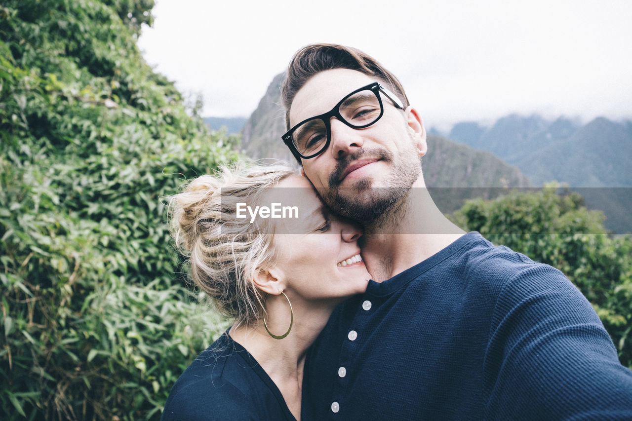 Portrait of man with girlfriend standing on mountain against sky