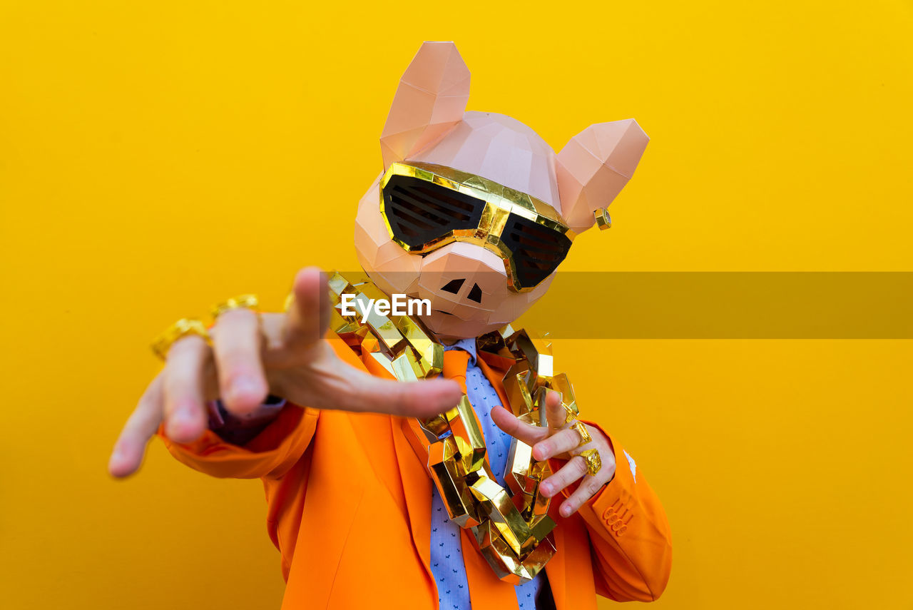 MIDSECTION OF MAN HOLDING YELLOW UMBRELLA AGAINST ORANGE BACKGROUND