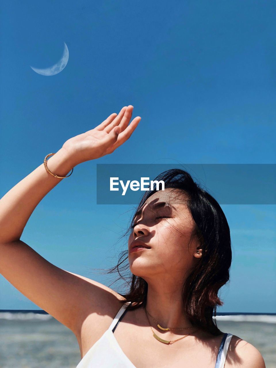 Young woman shielding eyes against blue sky