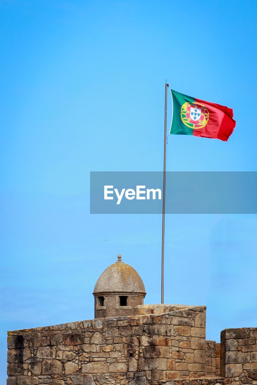 LOW ANGLE VIEW OF FLAG FLAGS AGAINST BUILDING AGAINST CLEAR BLUE SKY