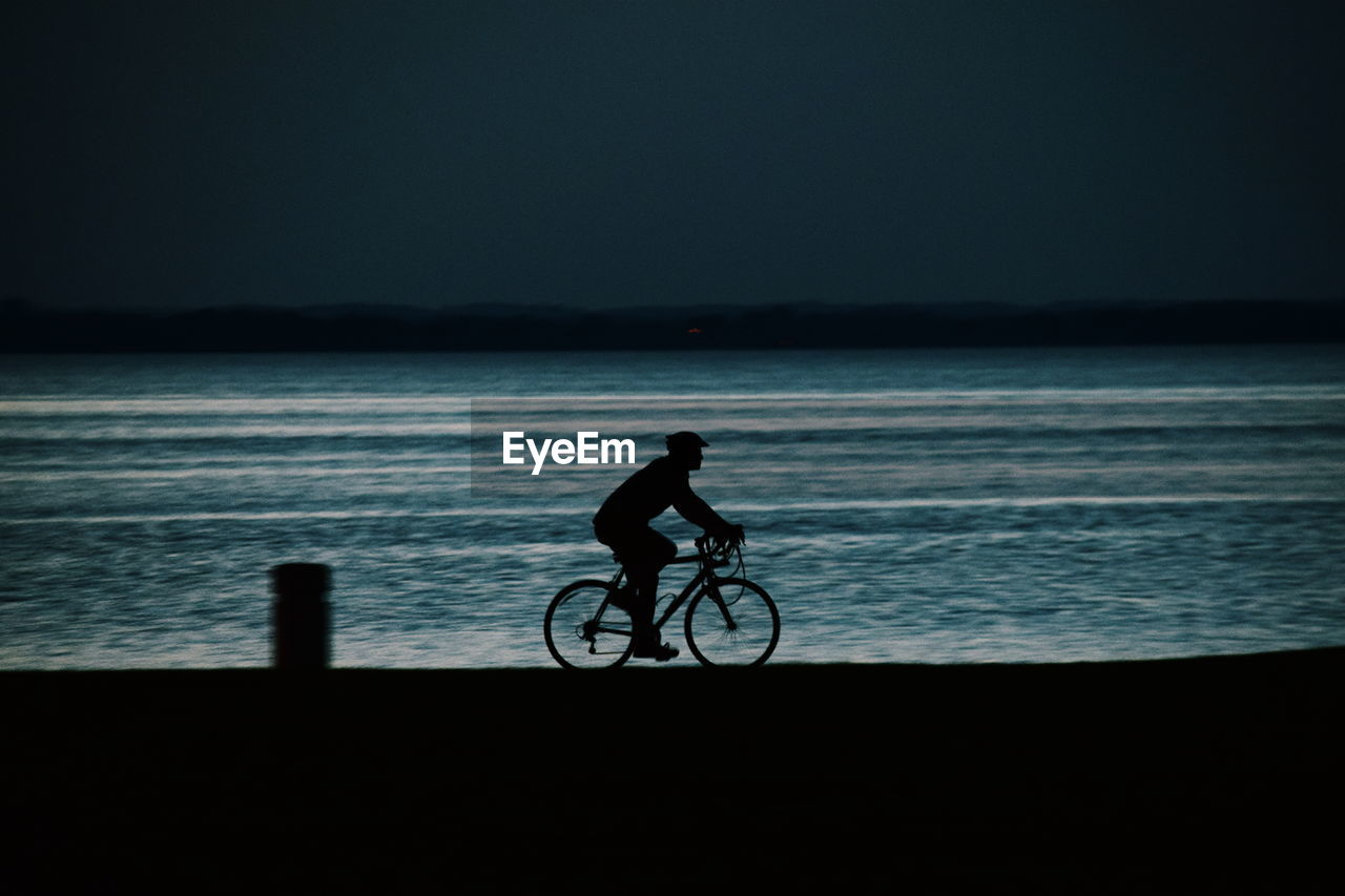 Silhouette of man cycling on shore at night