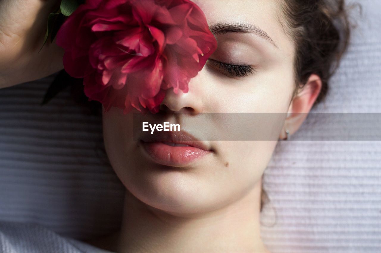 Directly above shot of young woman with pink flower lying on bed