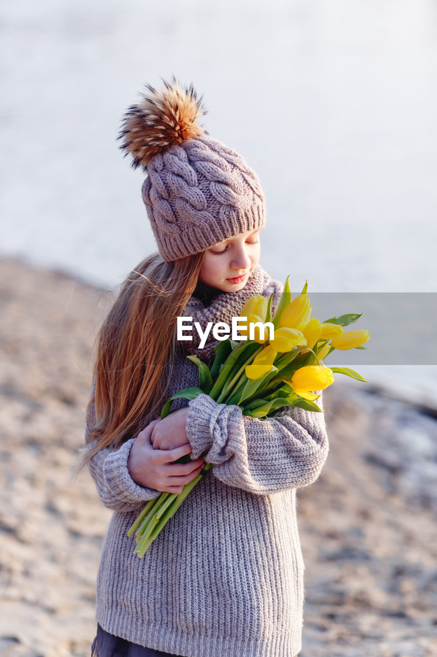 Cute girl holding tulip flower standing at lakeshore