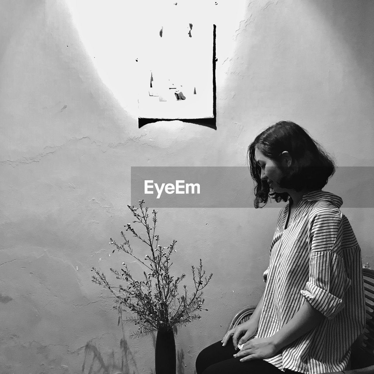 Side view of woman sitting by wall at home