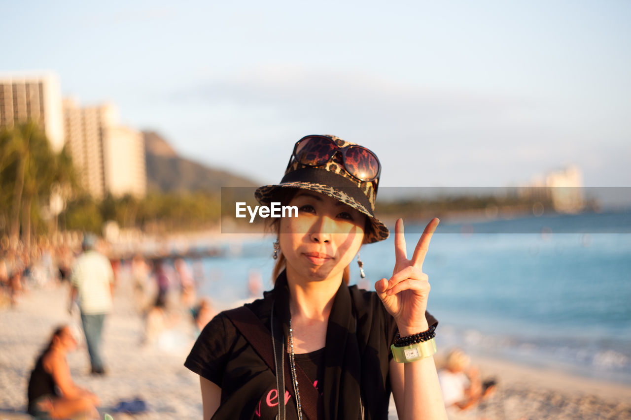 Close-up portrait of woman showing peace sign while standing at beach