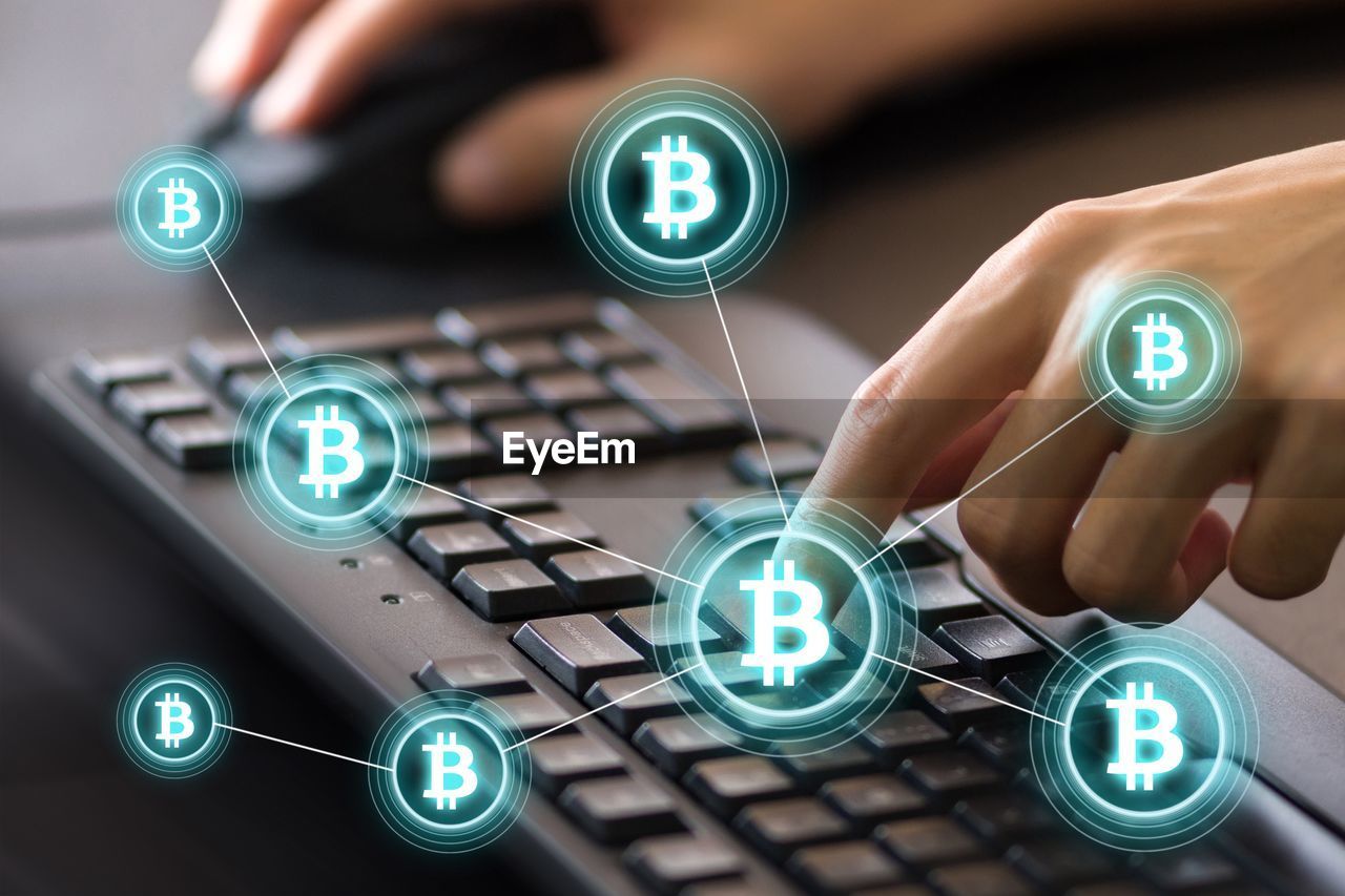 Digital composite image of cropped hands using computer keyboard by bitcoin icons