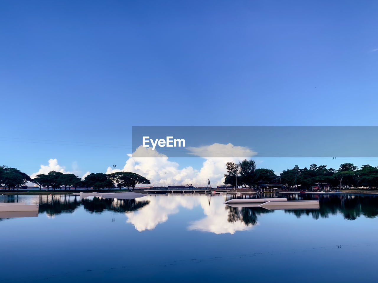 REFLECTION OF TREES IN LAKE AGAINST BLUE SKY