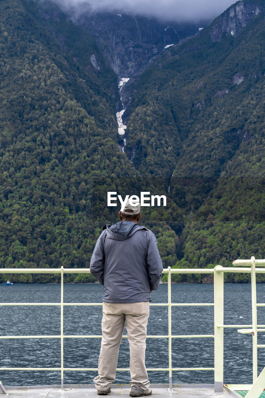 Rear view of man looking at lake against mountain