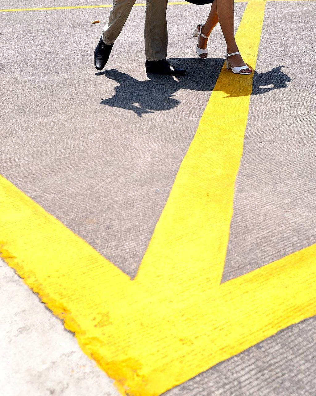 Low section of man and woman walking on road with marking