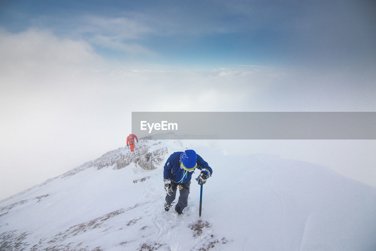 Hikers walking on snow covered mountains against sky