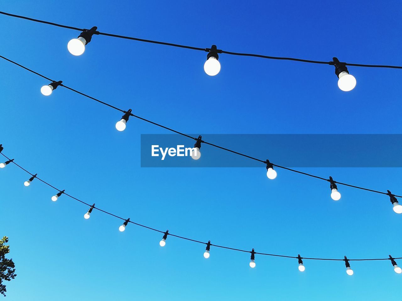 Low angle view of light bulbs hanging against blue sky