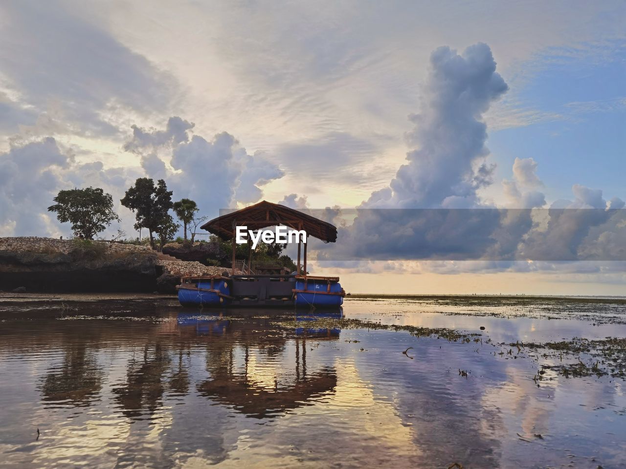 STILT HOUSE ON LAKE AGAINST SKY DURING SUNSET