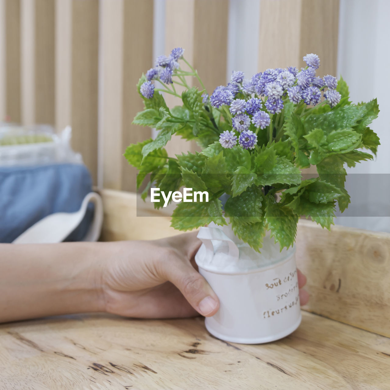 Close-up of hand holding purple flower vase on table