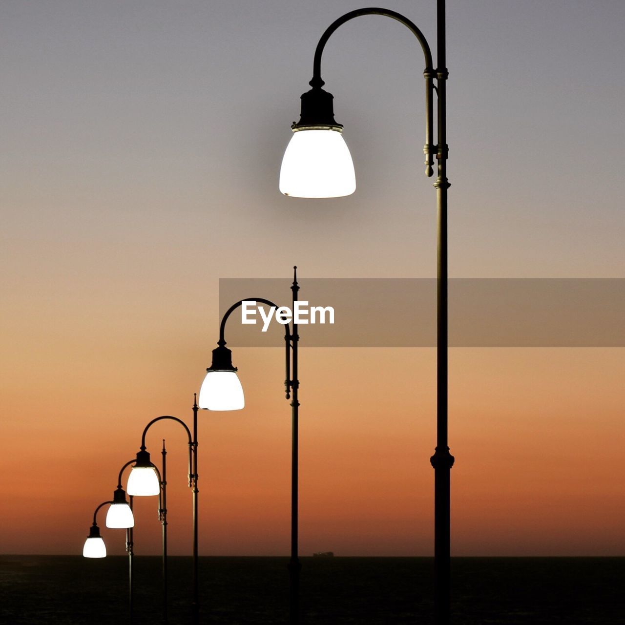 Illuminated street lights against clear sky during sunset