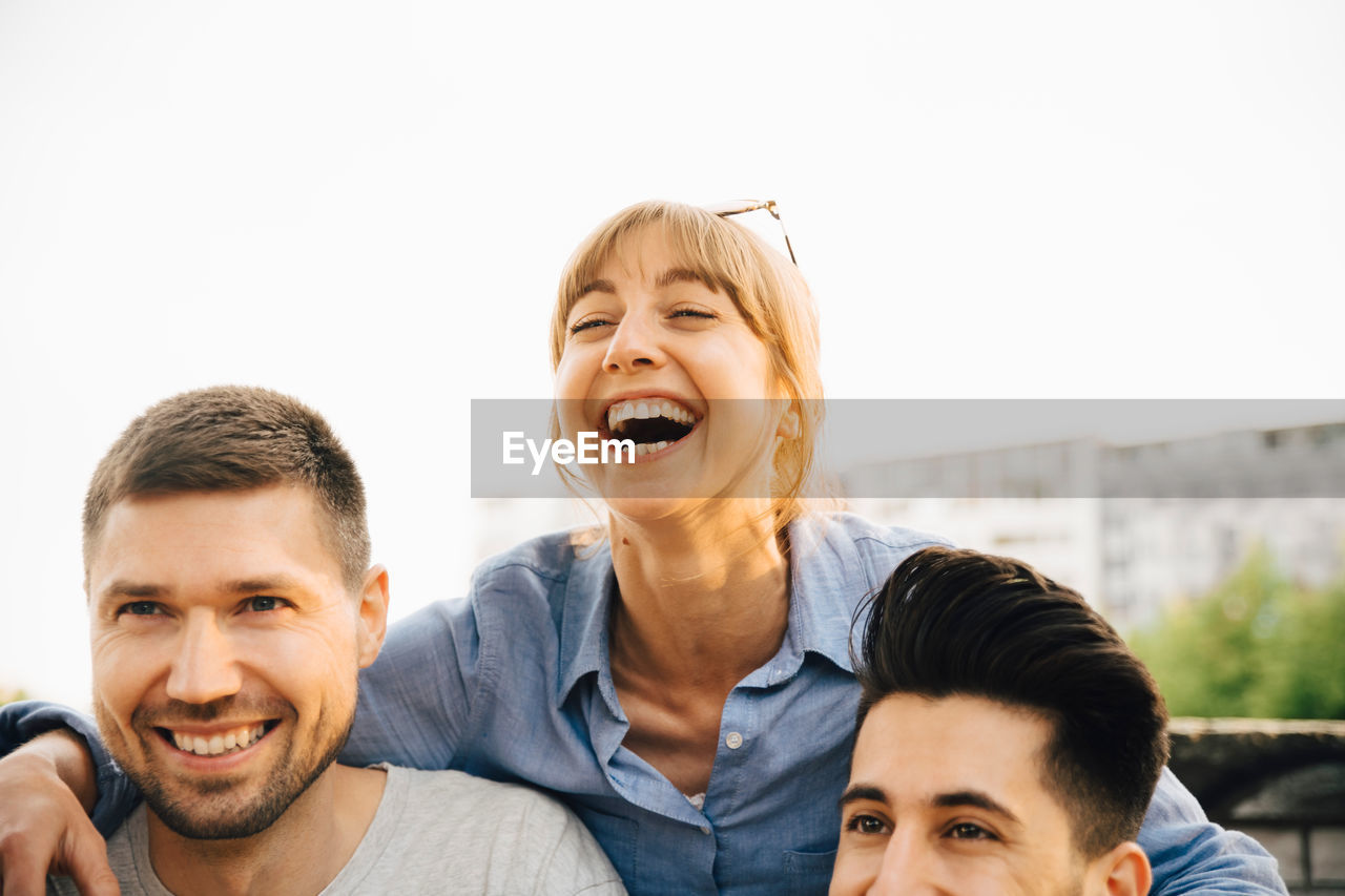 Mid adult woman laughing while standing by male friends at social gathering