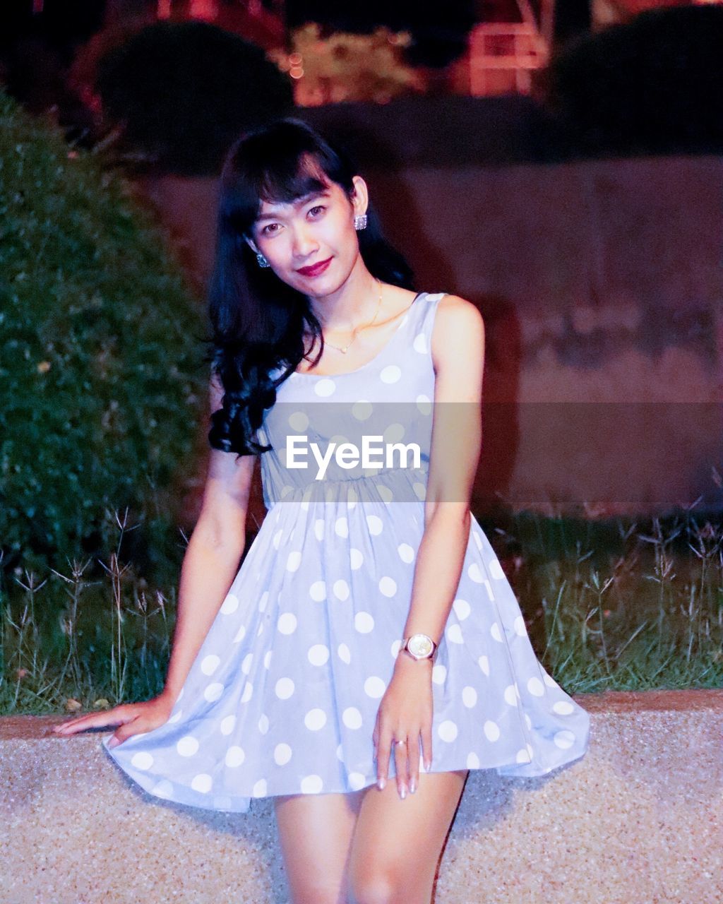 Portrait of young woman sitting on retaining wall at night