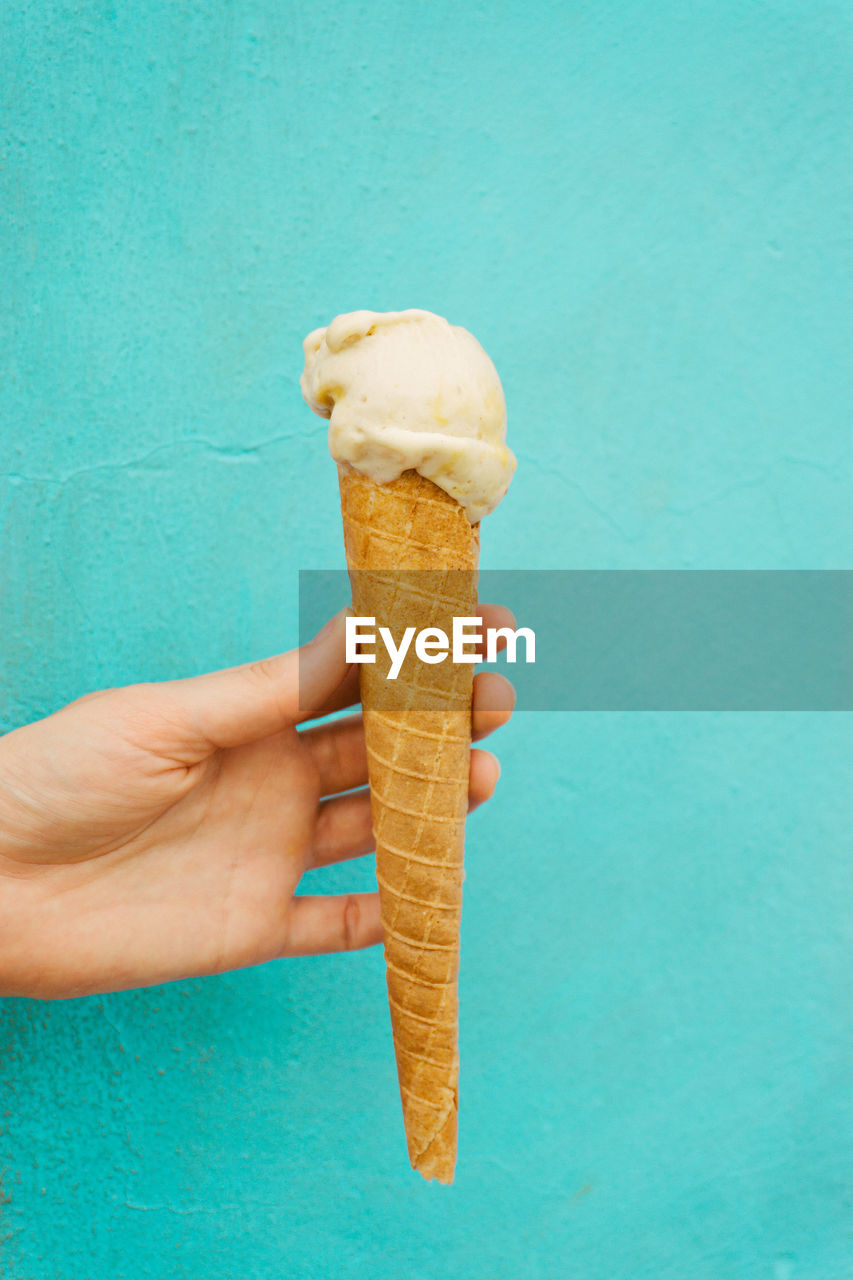 Cropped image of hand holding ice cream cone against blue wall