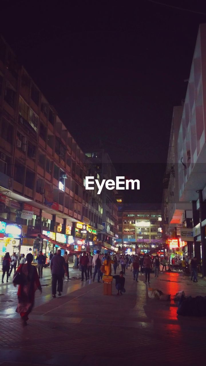 GROUP OF PEOPLE WALKING ON ILLUMINATED CITY STREET AT NIGHT