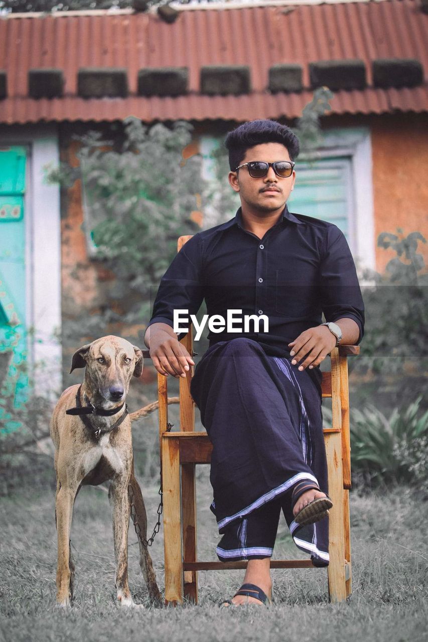 Full length of young man sitting on chair with dog outdoors