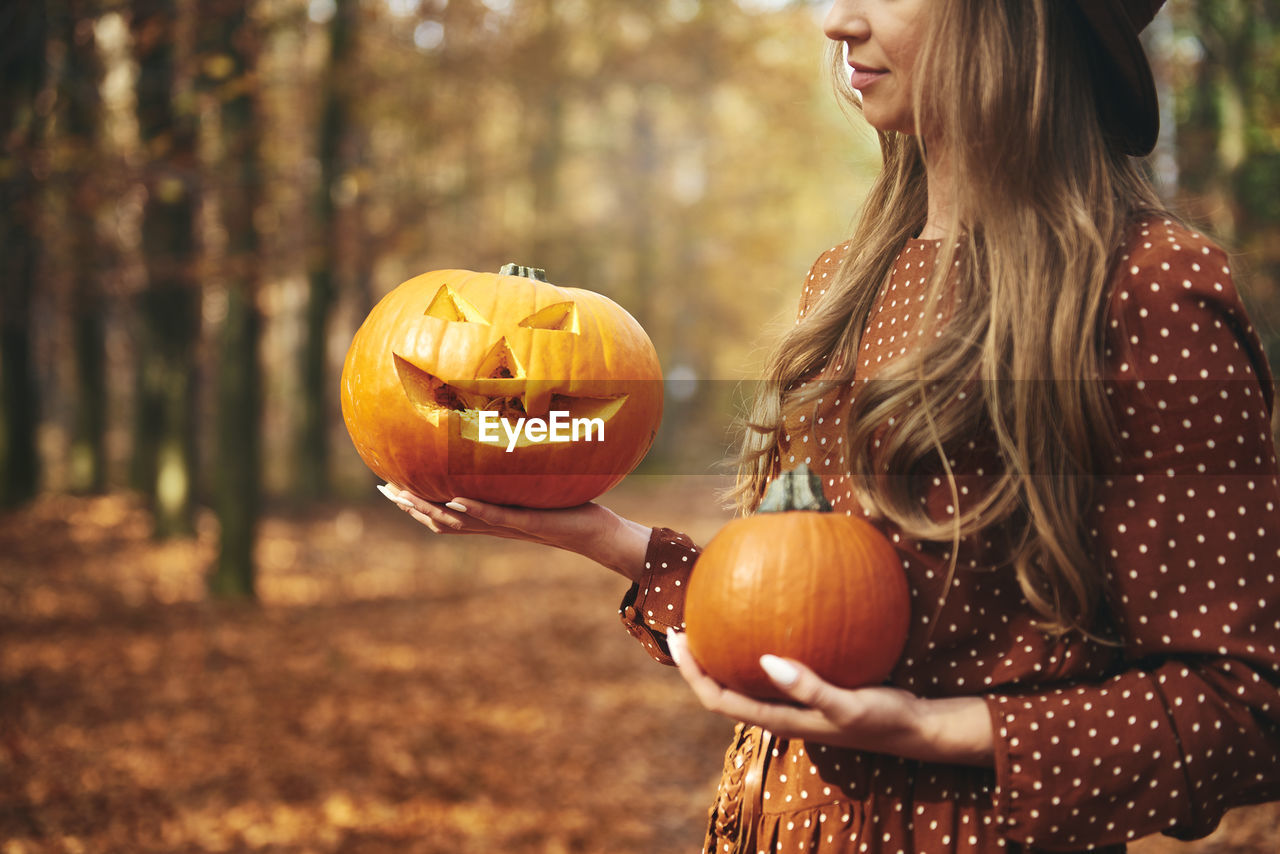 Midsection of woman holding jack o lantern and pumpkin during autumn