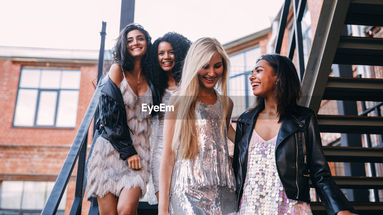 Low angle view of cheerful young female friends moving down on staircase against building
