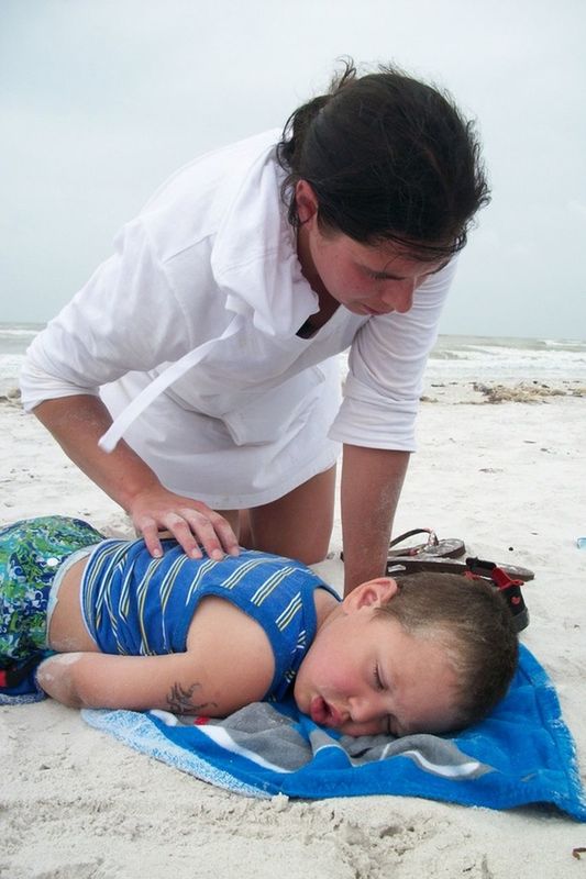 REAR VIEW OF MOTHER AND SON SITTING ON BEACH