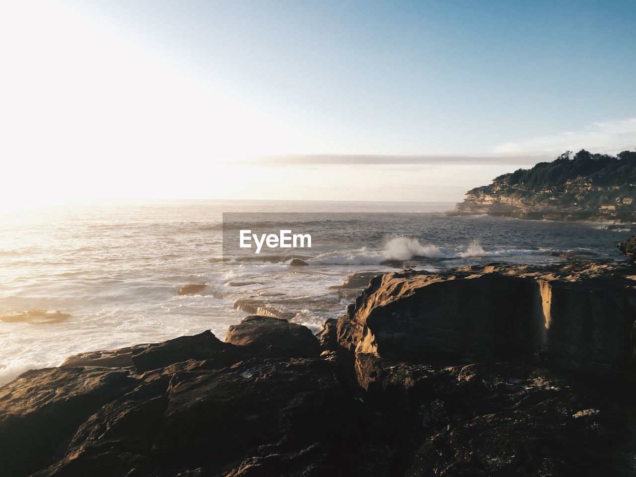 Scenic view of sea and rocky cliffs against cloudy sky